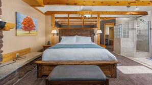 Une chambre avec un lit en bois, un banc, une table de chevet, un tableau et un espace douche.