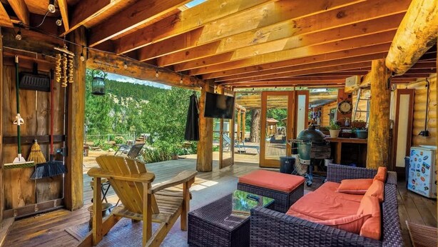 Une cabane en bois dotée d’un patio couvert, de meubles en osier et offrant une vue sur la forêt.