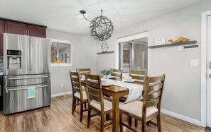 A modern kitchen with a stainless steel refrigerator, wooden dining table, and chairs. - Luxury Durango Retreat - Hot Tub, Views! (Durango)
