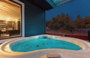 A hot tub with a control panel, a kitchen area visible through a sliding door, and a view of trees and shrubs. - Luxury Durango Retreat - Hot Tub, Views! (Durango)