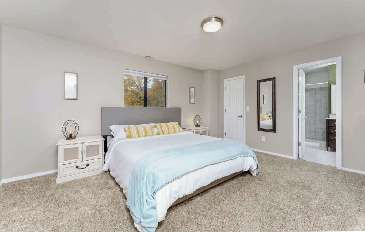 A bedroom with a bed, nightstands, a window, and a door leading to a bathroom.