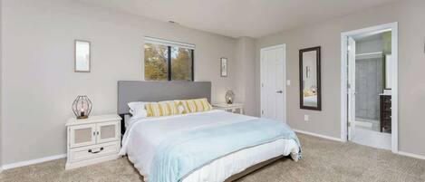 A bedroom with a bed, nightstands, a window, and a door leading to a bathroom.