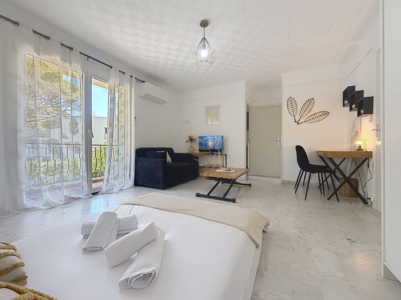 Habitación de hotel con cama, escritorio, sillón, sofá, televisión y balcón con cortinas.