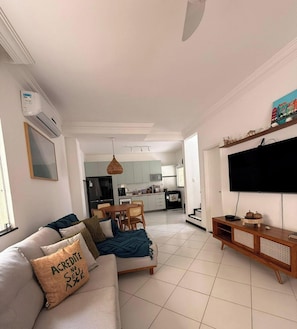 A modern living room with a sofa, TV, and a dining area in the background.