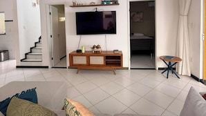 A modern living room with a flat-screen TV, a ceiling fan, a staircase, and a dining area. - Casa Arembepe - Camaçari-BA (Camaçari)