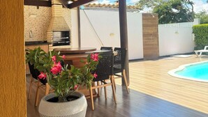 An outdoor kitchen area with a pergola, seating, and a pool. - Casa Arembepe - Camaçari-BA (Camaçari)