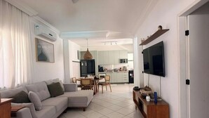 A modern living room with a sofa, TV, and dining area. - Casa Arembepe - Camaçari-BA (Camaçari)