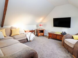 A loft-style room with a high ceiling, a flat-screen TV mounted on the wall, a wooden coffee table, a sofa, and a small side table.