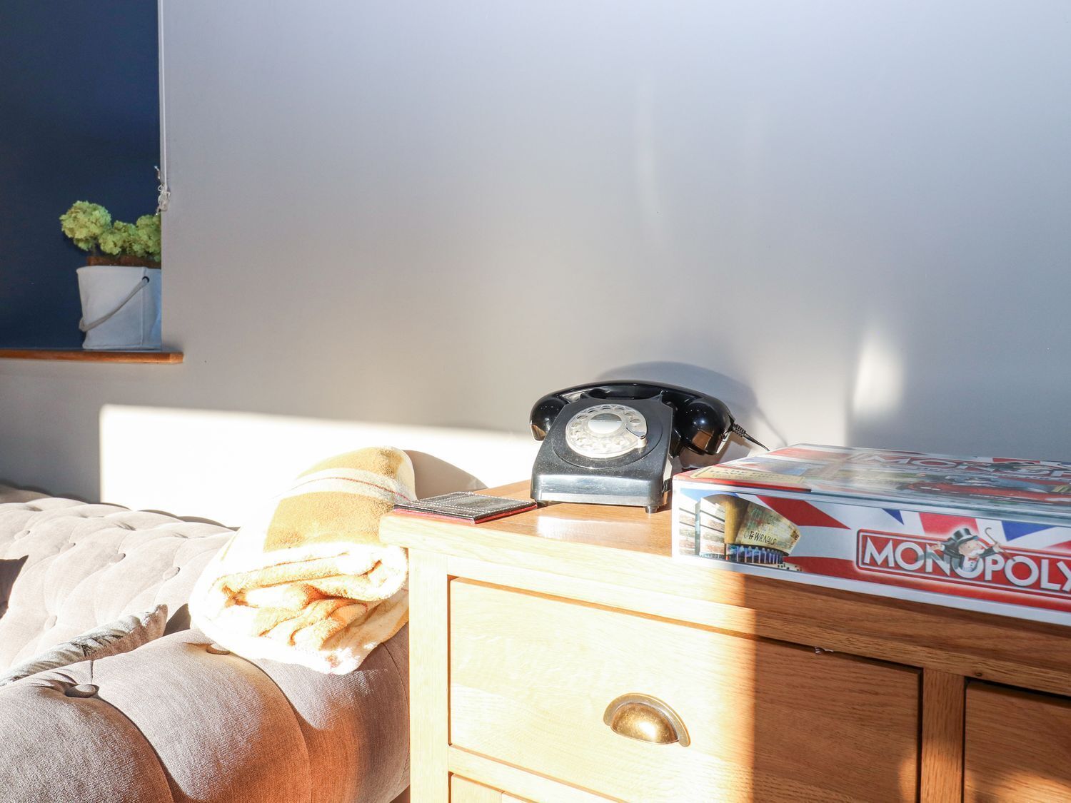 Un dormitorio con cama, mesita de noche con teléfono y caja del juego Monopoly.