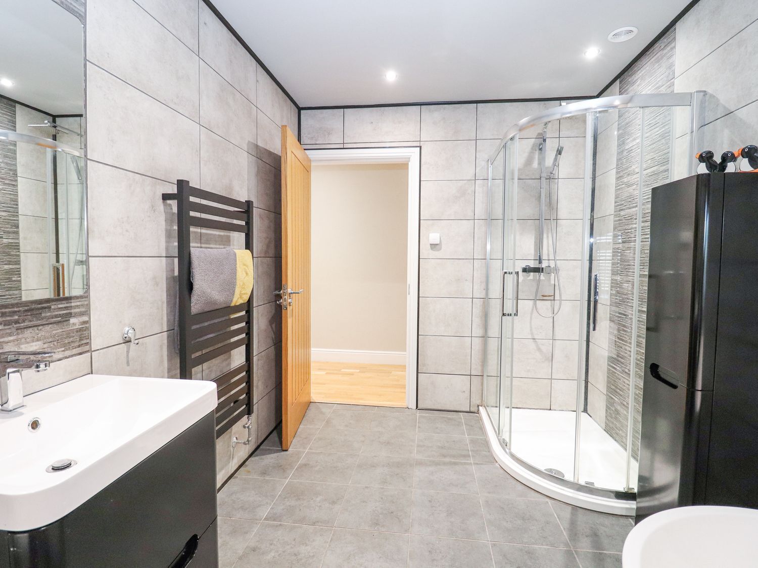 Un bagno moderno con box doccia in vetro, lavandino bianco e porta in legno.
