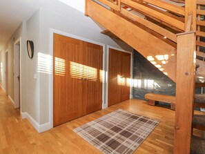 A staircase leading to an upper level, wooden floors, a plaid rug, and a door with a handle. - The Steading (Dumfries)