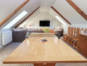 Una habitación con techos altos, una mesa de ping pong, un área de estar y un televisor.
