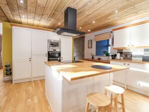 A modern kitchen with wooden flooring, white cabinetry, a central island, and a built-in oven. - The Steading (Dumfries)