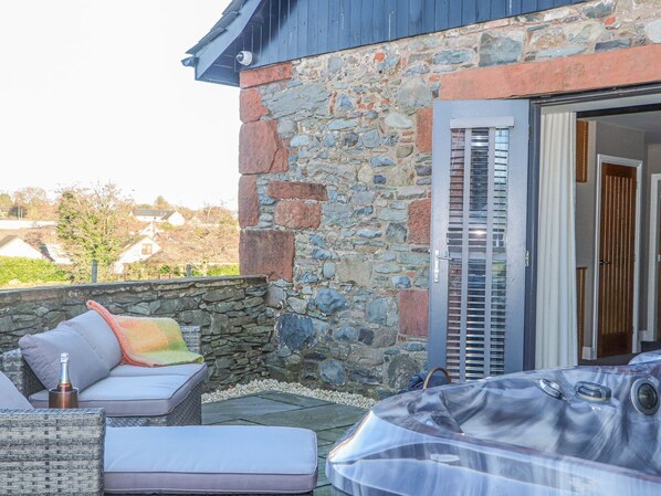 A stone building with a patio area featuring outdoor furniture and a hot tub.
