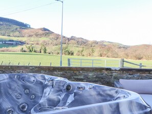 A hot tub with a stone wall and a view of a green field and hills. - The Steading (Dumfries)