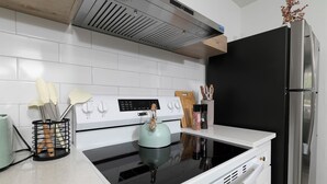 Una cocina con estufa, un refrigerador negro y una campana extractora sobre la estufa.