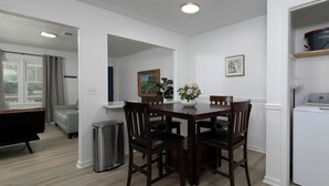 Un comedor con una mesa, sillas, un cubo de basura, un cuadro y un refrigerador.