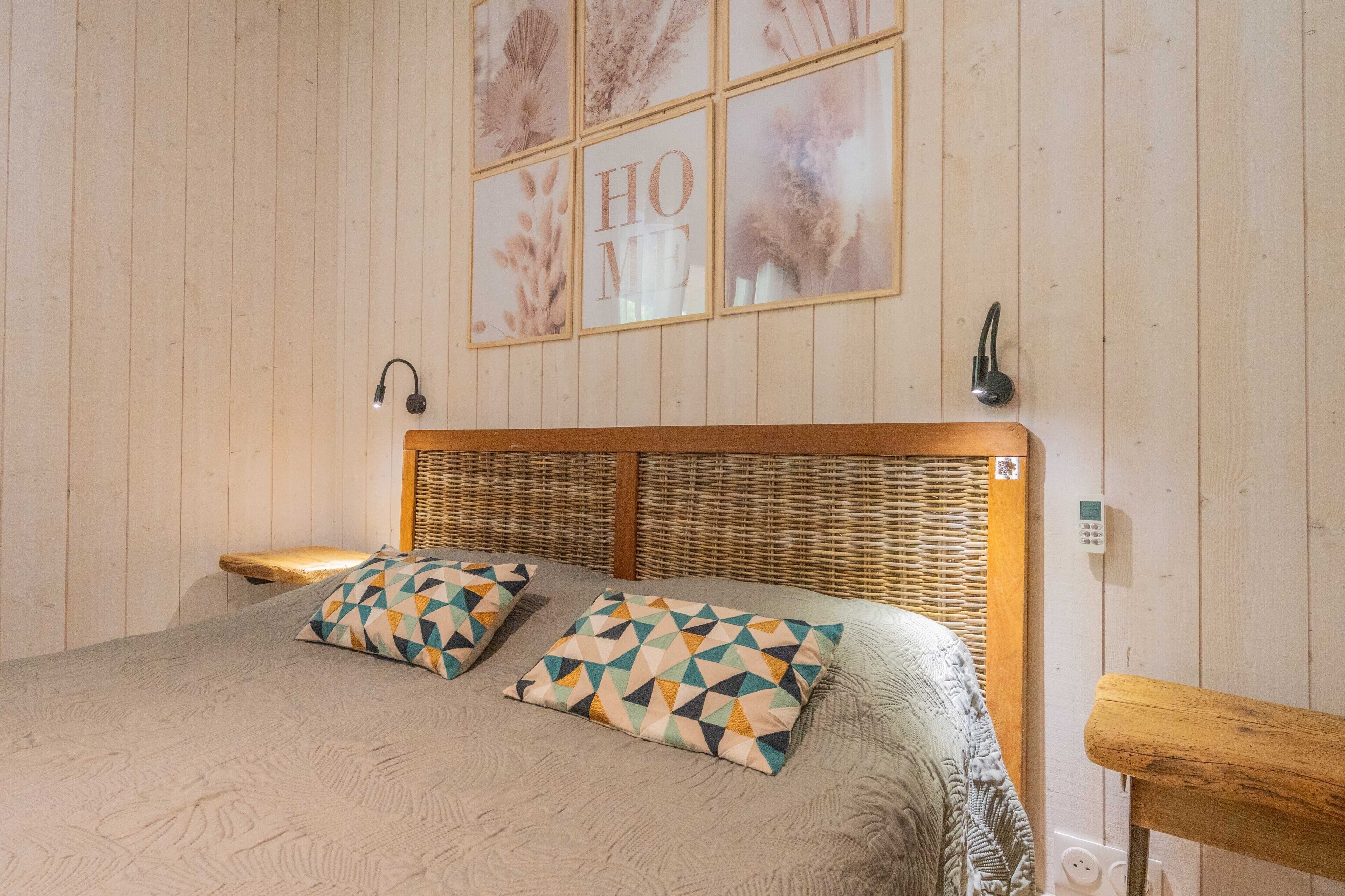 A bedroom with a wooden headboard, a bed with patterned pillows, a bedside table, and a wall-mounted light fixture.
