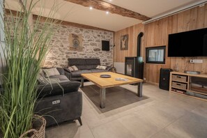 A living room with a sofa, a coffee table, a television, and a stone wall. - Gite - La grange Tima: Spacious House with Mountain Views for Groups (Orgeix)