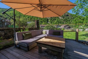 An outdoor deck with a wooden table and a cushioned bench under a large umbrella. - Gite - La grange Tima: Spacious House with Mountain Views for Groups (Orgeix)