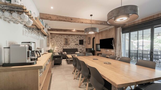 Eine moderne Küche mit einem Holztisch und -stühlen, einer Kaffeemaschine und einem an der Wand montierten Fernseher.