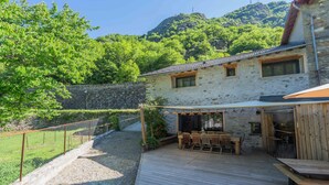 Ein Steinhaus mit einer Holzterrasse, Sitzgelegenheiten im Freien und einem Berg im Hintergrund.