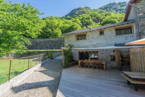A stone building with a wooden deck, outdoor seating, and a view of a mountainous landscape. - Gite - La grange Tima: Spacious House with Mountain Views for Groups (Orgeix)