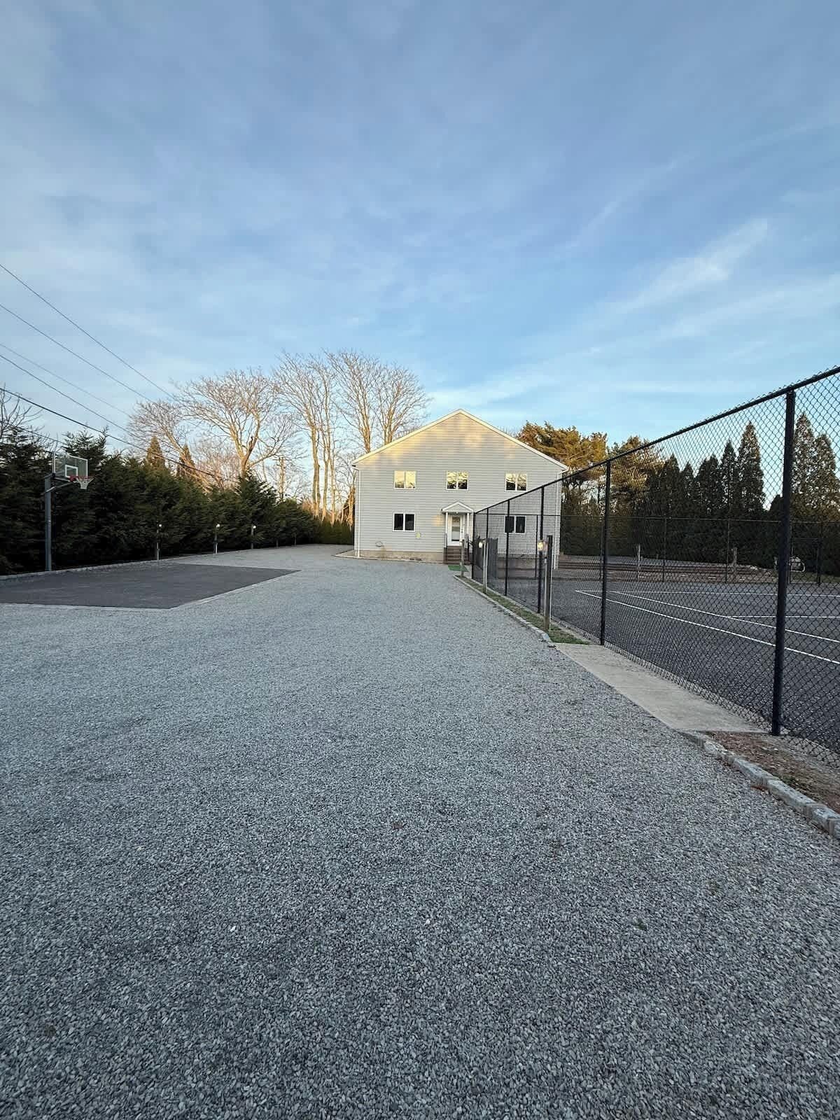A building with a basketball court, a fenced area, and a gravel driveway.