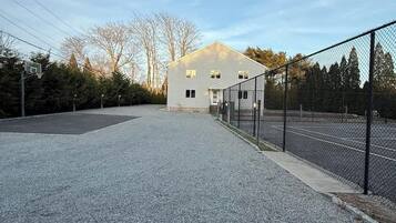 A building with a basketball court, a fenced area, and a gravel driveway.