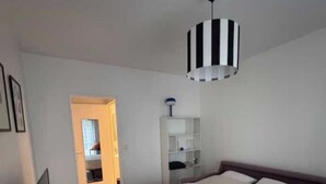 A bedroom with a bed, a desk, a chair, a checkered rug, and a hanging light fixture. - Vintage 2P Studio - Issy-les-moulineaux (Issy-les-Moulineaux)