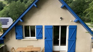 Une maison avec un toit en pente, une terrasse avec une table et des chaises, et une vue sur un paysage verdoyant.