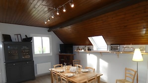 Un coin repas avec une table en bois dressée pour quatre personnes, un buffet sombre, un téléviseur et une lucarne.