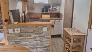 Eine kompakte Küche mit Steinrückwand, Holzschränken, einem eingebauten Herd und einem kleinen Holztisch mit Schneidebrett mit Blumenmuster.