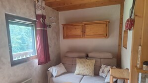 Ein gemütliches Zimmer mit einem Holzschrank, einer gepolsterten Couch mit gemusterten Kissen, einem kleinen Holztisch und einem Heizkörper.