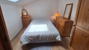 Ein Schlafzimmer mit Dachfenster, einem Bett, einem Schminktisch, einem Spiegel und einem Nachttisch.