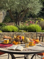 Una mesa de comedor al aire libre con un libro, una cesta de frutas, una botella de jugo y una taza.