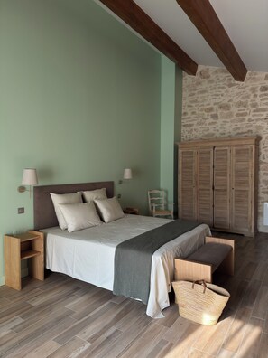 A bedroom with a bed, bedside tables, a chair, a wardrobe, and a large woven bag. - Moulin de Carrière (Uzès)