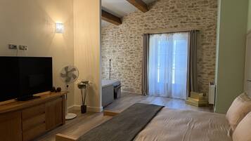 A bedroom with a bed, a TV, a fan, and a stone wall.
