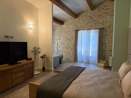 A bedroom with a bed, a TV, a fan, and a stone wall.