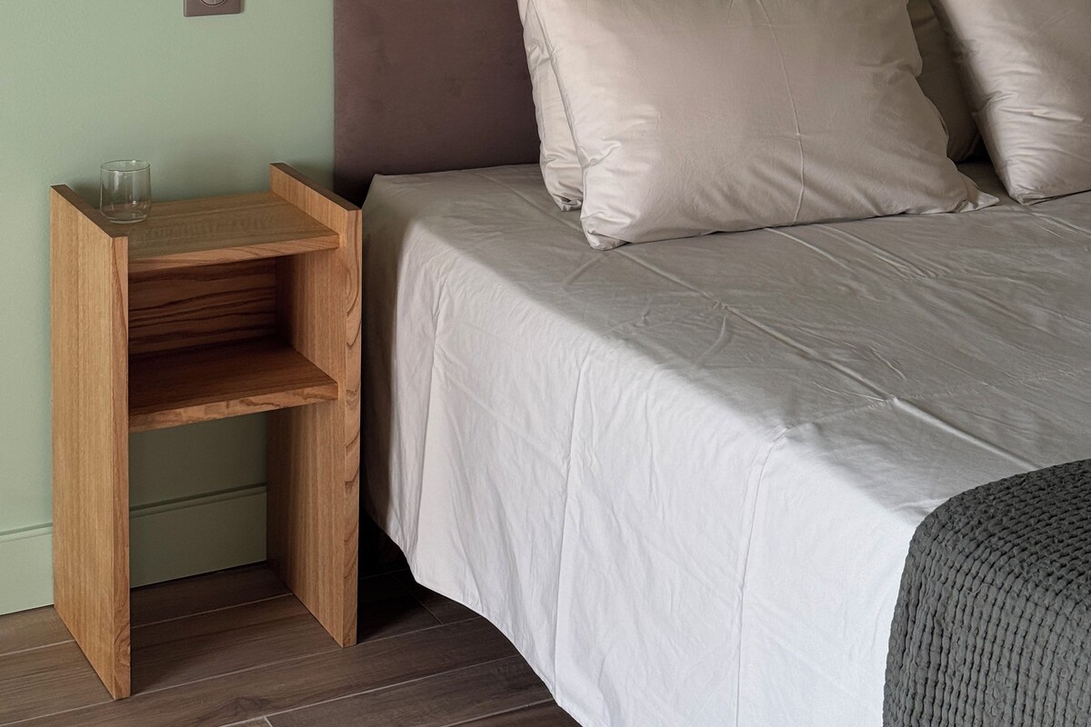 A bed with a headboard, a bedside table with a lamp, and a wall-mounted switch.