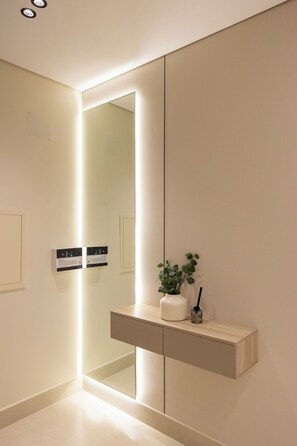 A modern bathroom with a mirror, a lighted wall panel, a shelf with a plant, and a wall-mounted control panel. - Premium Stay Near the Haram Peace & Convenience (Madinah)