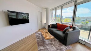 Ein modernes Wohnzimmer mit einem großen Fenster, einem Flachbildfernseher, einem grauen Sofa und einem gemusterten Teppich.