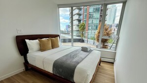 Ein modernes Schlafzimmer mit großem Fenster, einem Holzbett und Blick auf eine Stadtlandschaft.