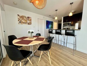 Una cocina moderna con electrodomésticos de acero inoxidable, un comedor con mesa redonda y sillas negras, y una lámpara colgante.