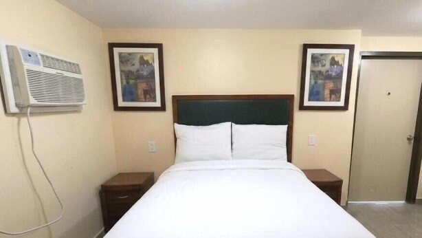 A hotel room with a single bed, two bedside tables, a wall-mounted air conditioner, and two framed pictures on the walls. - GG Rest Inn (Elizabeth)