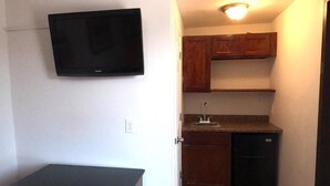 A compact kitchen with a built-in dishwasher, wooden cabinets, and a wall-mounted TV. - GG Rest Inn (Elizabeth)