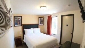 A hotel room with a bed, a nightstand, a door, and two framed pictures on the wall. - GG Rest Inn (Elizabeth)