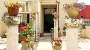 Une cour intérieure avec des colonnes soutenant de grands pots de fleurs, un escalier et l’entrée d’un bâtiment.