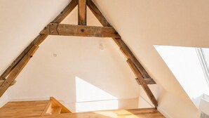 Ein Zimmer mit schrägverdeckter Decke, Holzbalken und Holzboden.