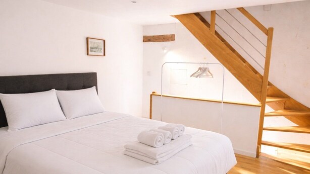 Ein Schlafzimmer mit einem Bett, Kissen, einer Holztreppe und einem gerahmten Bild an der Wand.